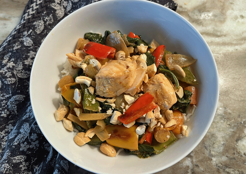 Bowl of salmon, and vegetables over rice in a red curry sauce.  
