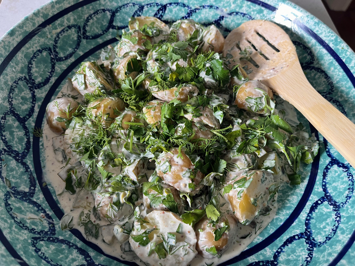 Blue bowl with bamboo spoon. Potatoes in a creamy sauce with fresh dill and parsley sprinkled on top.
