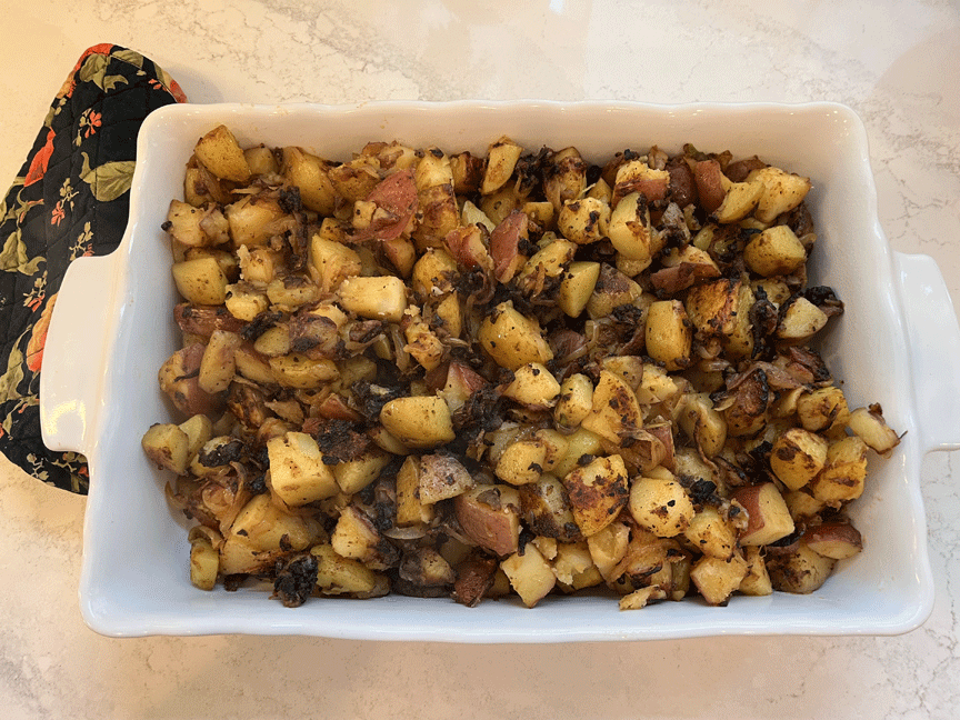 White serving dish showing roasted cubes of potatoes with onions and seasonings.