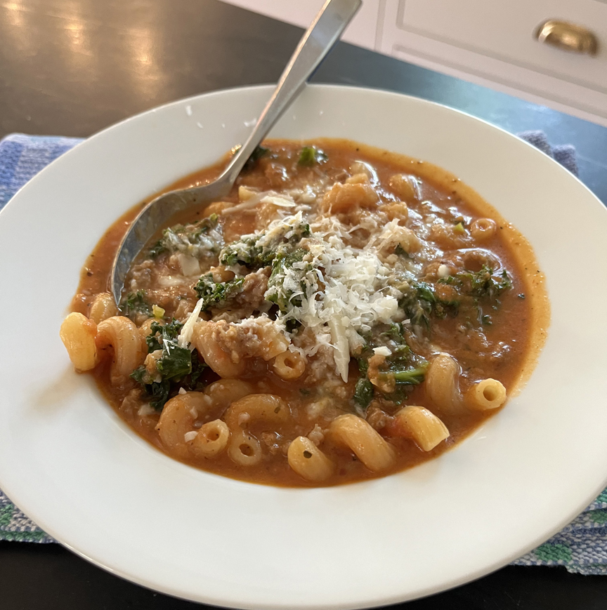 white bowl full of soup with noodles, grated cheese and kale. 