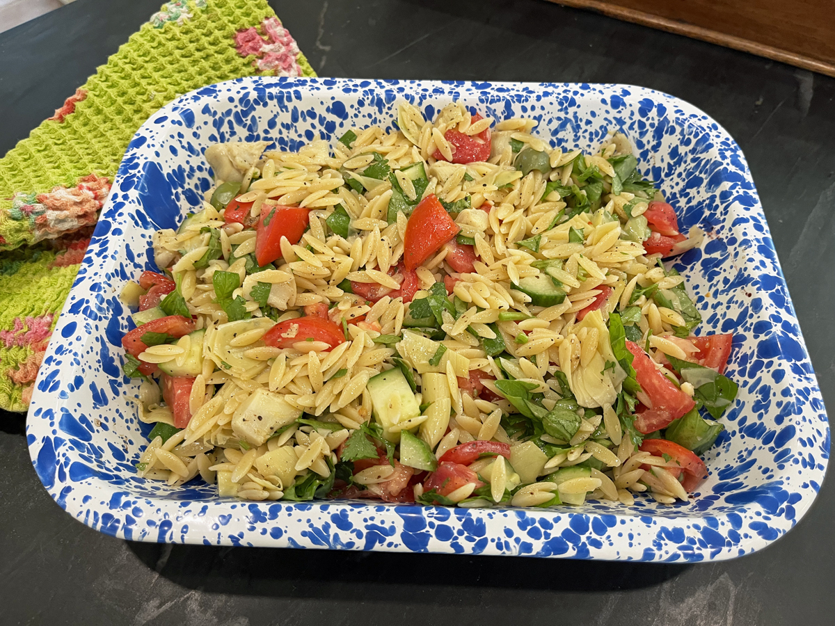 Orzo with tomatoes, cucumber and a dressing in a speckled blue rectangular dish.